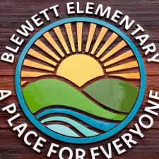 A wooden school sign with a circular logo of mountains and trees that reads, "Blewett Elementary - A Place for Everyone."