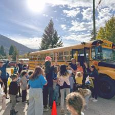 Children and adults cheering beside a school bus on a sunny day.