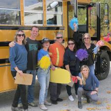 Elementary school staff pose with a bus driver in front of his school bus.
