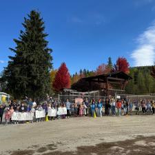 A large group of children and adults cheering in front of an elementary school on a sunny day.